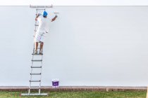 Giovane pittore irriconoscibile che dipinge la facciata di un appartamento con un rullo dalla scala — Foto stock