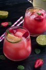Du dessus de verres d'eau de coco froide avec tranches de citron vert et fraises servis sur une table en bois sombre — Photo de stock