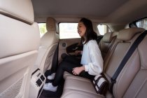Crop positivo passeggero etnico femminile in abbigliamento formale con smartphone che chiude la portiera dell'auto dal sedile posteriore — Foto stock
