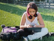 Mujer seria sentada con las piernas cruzadas en el césped cubierto de hierba y el teléfono inteligente de navegación - foto de stock