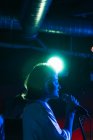 Уверенная дама с гитарой поет в микрофон, исполняя песню в ярком клубе с неоновым светом — стоковое фото