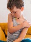 Kranker Junge misst Temperatur mit elektronischem Thermometer, während er zu Hause auf der Couch sitzt und Grippe hat — Stockfoto