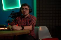 Junger männlicher Radiomoderator in kariertem Hemd und Kopfhörer sitzt mit Mikrofon am Tisch und kommuniziert mit einem anonymen Kollegen während der Podcast-Aufzeichnung im Studio — Stockfoto