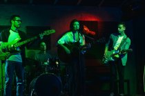 Gruppo di persone in abiti casual che suonano chitarre e tamburi mentre la donna canta ed esegue canzoni in club con luci al neon — Foto stock