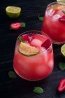 Du dessus de verres d'eau de coco froide avec tranches de citron vert et fraises servis sur une table en bois sombre — Photo de stock