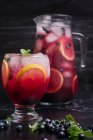 Bicchiere e brocca con rinfrescante limonata fredda con mirtilli freschi e fette di limone poste su tavolo scuro — Foto stock