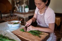 Von oben hacken Frauen frische grüne Kräuter auf einem Holzschneidebrett, während sie in der Küche das Abendessen zubereiten — Stockfoto