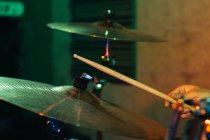 Recadré musicien masculin concentré méconnaissable jouant de la batterie dans le club avec éclairage au néon vert et bleu — Photo de stock