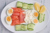 From above of smoked salmon and cream cheese served on plate with boiled eggs and cucumber slices for tasty lunch — Stock Photo