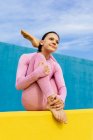 Jeune femme coûteuse faisant variation de pose bébé berceau tout en méditant dans le yoga asana sur fond bleu et jaune — Photo de stock