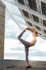 Full body of active female in sportswear performing standing split with bent knee while standing on one leg near photovoltaic panel on street — Stock Photo