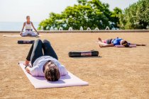 Інструктор йоги сидить у лотосі, а люди лежать на килимах під час шавазани в парку в сонячний день. — стокове фото