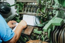 Безрастительный безликий работник среднего возраста кладет кучу бумаги в старую машину для резки металла на заводе — стоковое фото