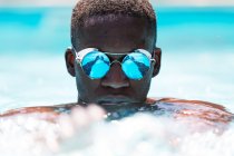 Calmo afro-americano masculino em óculos de sol elegantes com reflexo de água nadando na piscina contra fundo borrado no dia ensolarado de verão — Fotografia de Stock