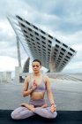 Cuerpo completo de mujer pacífica en ropa deportiva con los ojos cerrados practicando la postura Padmasana en la calle contra el panel solar moderno en la ciudad - foto de stock