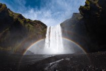 Cenário de tirar o fôlego do arco-íris brilhando sobre a poderosa cachoeira Skogafoss que flui através de penhasco rochoso na Islândia — Fotografia de Stock