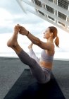 Ganzkörper-Seitenansicht einer sportlichen Frau in Aktivkleidung, die Ubhaya Padangushthasana-Haltung in der Nähe moderner Photovoltaik-Panels beim Yoga-Training auf der Straße praktiziert — Stockfoto