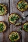 From above of cauliflower and walnut cakes with greens near fork on planked wooden table — Stock Photo
