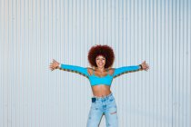 Full body of stylish female in trendy outfit with top looking at camera while standing with arms outstretched against white background on street and smartphone sticking out of his pants pocket — Stock Photo