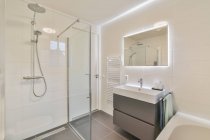Раковина и туалет расположены рядом с ванной за стеклянной стеной в светлом туалете дома — стоковое фото