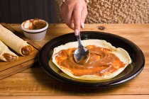 Crop faceless female spreading sweet Dulce de leche oh fresh crepe served on black plate on wooden table in kitchen — Stock Photo