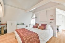 Cómoda cama suave con ropa de cama blanca y almohadas de colores en el elegante dormitorio en el apartamento moderno - foto de stock