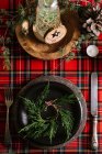 From above Christmas table setting with wreath on ceramic plate with cutlery on red checkered tablecloth on the background — Stock Photo