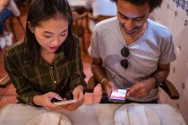 Felice giovane coppia multirazziale in abiti casual utilizzando smartphone mentre seduti insieme a tavola nel ristorante moderno — Foto stock