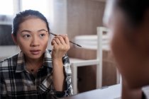 Konzentrierte charmante ethnische Frau, die Augenbrauenstift aufträgt, während sie Make-up macht und in den Spiegel schaut — Stockfoto