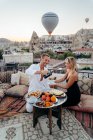 Von oben der fröhliche Mann serviert Tee für Frau beim romantischen Date auf der Dachterrasse gegen den malerischen Blick auf die Altstadt mit Heißluftballons fliegen — Stockfoto