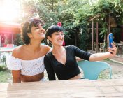 Зміст дружніх багаторасових жінок, які роблять самостріл на мобільний телефон, насолоджуючись вихідними разом у літньому парку — стокове фото