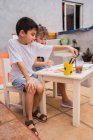 Crianças positivas com pincéis pintura com aquarelas coloridas sobre papel à mesa com suprimentos em sala de luz com quadro branco — Fotografia de Stock