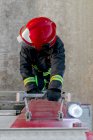 De cima de um bombeiro anônimo usando capacete protetor vermelho e uniforme em pé na escada do caminhão de bombeiros e olhando para longe — Fotografia de Stock