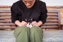 Crop femelle méconnaissable embrassant bébé chat mignon tout en étant assis sur le banc dans la journée par temps venteux — Photo de stock