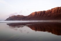 Vista panorámica de la playa de Famara contra el monte y el océano bajo el cielo nublado en Teguise Lanzarote Islas Canarias España - foto de stock