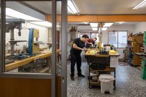 Artesãos focados luthiers trabalhando na própria oficina de reparação de guitarras elétricas com diferentes equipamentos profissionais e paredes de vidro — Fotografia de Stock