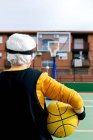 Anonymer Sportler in Aktivkleidung steht auf öffentlichem Sportplatz mit gelbem Ball und Basketballkorb beim Spiel auf der Straße — Stockfoto