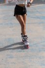 Анонимные женские ноги на белых роликах с розовыми колесами, стоящими на бетонном тротуаре в скейт-парке — стоковое фото