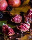 Parts of fresh red pomegranate placed on dark wooden table with autumn leaves — Stock Photo