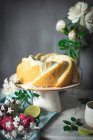 Gâteau au citron vert savoureux servi sur assiette blanche près des fleurs et des tranches de citron vert — Photo de stock