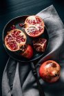 Top view of halved and whole ripe pomegranate on frying pan placed on creased stablecloth on table — стоковое фото