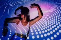 Donna alla moda in crop top sperimentando la realtà virtuale in cuffia mentre ballava nelle luci del proiettore — Foto stock