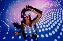 Mulher na moda no topo da colheita experimentando a realidade virtual no fone de ouvido enquanto dança em luzes do projetor — Fotografia de Stock