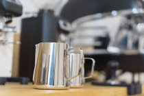 Weicher Fokus der Edelstahl-Profi-Kannen zum Ausschenken von Milch auf Holztheke in modernem Kaffeehaus mit Kaffeemaschine — Stockfoto