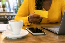 Anónimo afroamericano freelancer con tarjeta de crédito sentado en la mesa con netbook mientras hace la compra en línea en la terraza en la cafetería - foto de stock