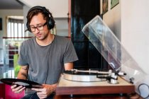 Орієнтований чоловік в окулярах слухає музику в навушниках від гравця в просторій квартирі — стокове фото