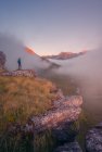 Blick zurück auf entfernte unkenntliche Touristen, die auf grasbewachsenem Gelände stehen, umgeben von rauen Bergen in der Natur Spaniens bei nebligem Wetter — Stockfoto
