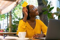 Позитивна афро-американська жінка-фрилансер з кредитною карткою сидить за столом з нетбуком під час онлайн-покупки на терасі в кафе. — стокове фото