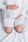 Dall'alto anonimo giovane incinta dolce femmina toccando pancia mentre seduto sul letto — Foto stock