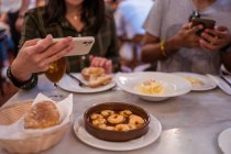 Зверху врожаю анонімна жінка фотографує смачну їжу з тарілками на смартфоні, обідаючи з хлопцем в ресторані — стокове фото